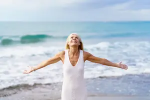 Beautiful mature woman demonstrates a simple beach ritual of thankfulness.