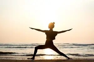 Young woman in warror pose gaining the benefits of beach yoga.