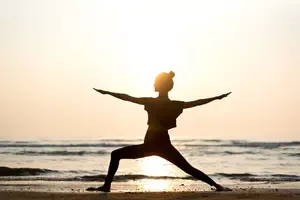 Young woman in warror pose gaining the benefits of beach yoga.