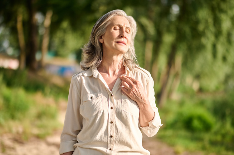 Mature woman giving thanks to the forest during her gratitude walk.