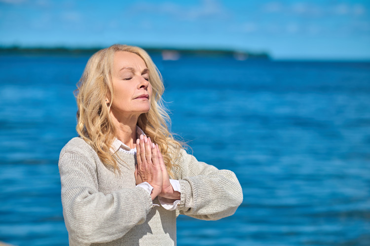 Mature woman standing meditation opn seashore to enhance earthing at the beach. Mature woman standing meditation opn seashore to enhance earthing at the beach.