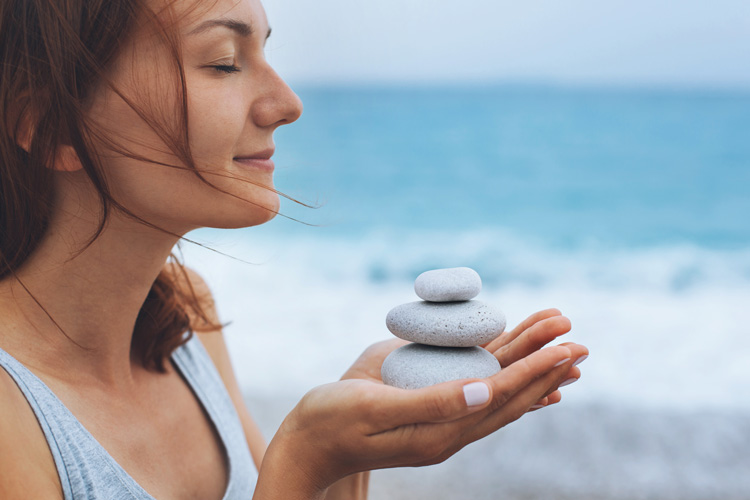 Beautiful mature woman with light blue zen stones participates in simple beach ritual for emotional healing. Beautiful mature woman with light blue zen stones participates in simple beach ritual for emotional healing.