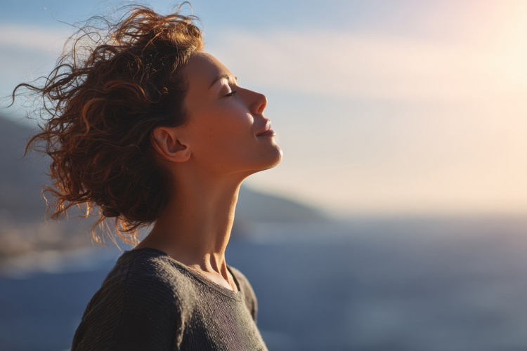 Mature woman meditating outdoors in the morning by the ocean.