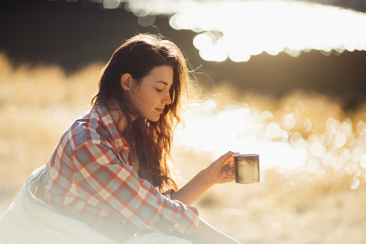 Young woman sipping herbal tea on a clear mountain morning to connect with the nature therapy aspect of Taos.