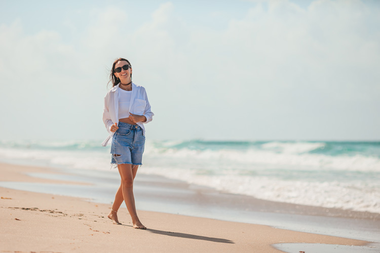 Grounding is one of the key spiritual benefits of the beach. Young woman walks barefoot.