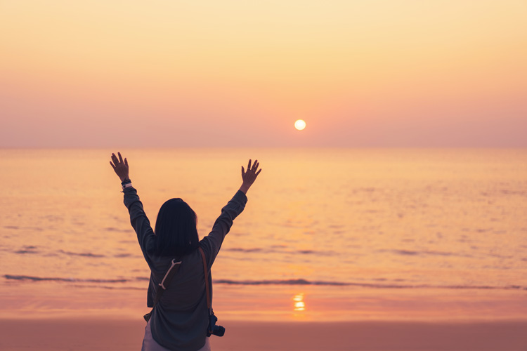 Young woman raises hands in celebration of Nature at the beach.
