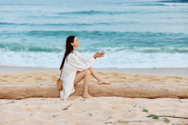 Young woman gives thanks on a driftwood log at the beach.