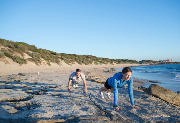 Young couple achieving the wellness benefits of the beach with push-ups.