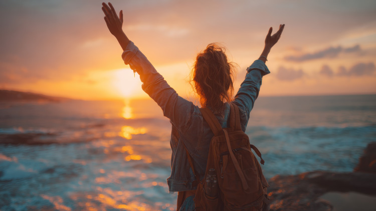Young woman connecting with nature at the beach by celebrating a sunset.