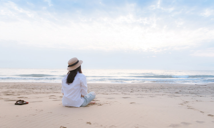 Young woman practicing mindfulness by watching the repetitive motion of the waves on a serene beach.