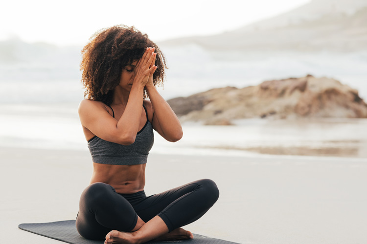 Young African-American woman demonstartes thankfulness during her beach yoga session.